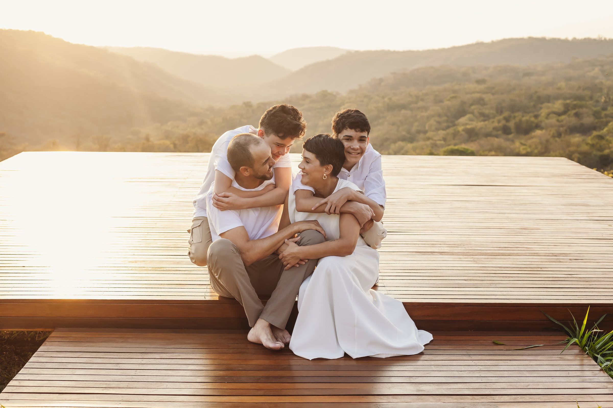 Ana Laura e Adolfo abraçados com a família sobre um deck de madeira, ao pôr do sol